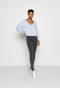 Pullover azul claro em V com mangas largas, combinado com jeans skinny pretos e ténis brancos. Conjunto simples e casual com um ajuste descontraído.