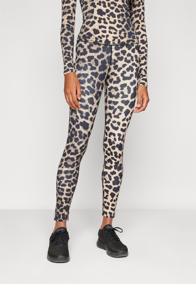 Leggins s tigrastim vzorom v bež in črni barvi, izdelani iz gladkega in elastičnega materiala. V kombinaciji s črnimi športnimi čevlji.