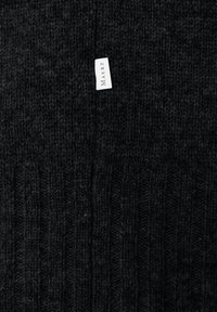 Czarna, dziana tkanina z białą, prostokątną metką, na której wyśrodkowano nazwę marki "MAERZ".