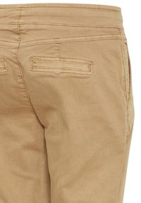 Pantalones de algodón beige con una textura suave, que cuentan con dos bolsillos traseros con solapas rectangulares y costuras en contraste.