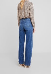 Jeans de mezclilla azules de tiro alto, con un corte relajado, que cuentan con bolsillos traseros y un ligero desvanecimiento. Se combinan con una blusa de estampado de leopardo.