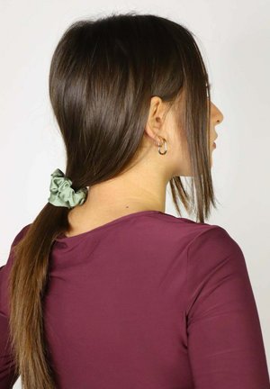 Jedwabna zielona gumka trzyma brązowy kucyk; osoba ma na sobie bordową koszulę z długim rękawem. Włosy są proste z lekką falą.