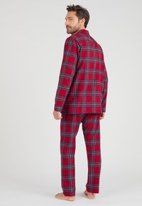 Set di pigiama in plaid rosso realizzato in tessuto morbido, composto da una camicia con bottoni e pantaloni abbinati con dettagli blu e neri. Vestibilità comoda, lunghezza completa.