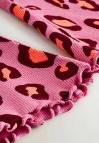 Tissu rose à côtes avec des taches en forme de cœur marron foncé et corail, bordé d'un volant. Texture douce, motif ludique.