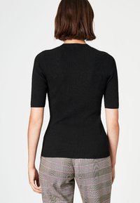 Musta ribbineulottu lyhythihainen paita, jossa istuva malli ja pyöreä pääntie, yhdistetty monivärisiin, ruutukuosisiin housuihin.