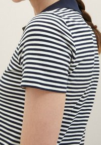 Námořnické a bílé pruhované polo tričko s límečkem, krátkými rukávy a žebrovanou strukturou. Obsahuje tmavý límeček a slim fit design.