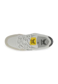 Baskets blanches de sport avec des côtés perforés, des lacets noirs, un accent jaune et un logo sur la languette. Présentant une semelle rembourrée et des textures lisses.