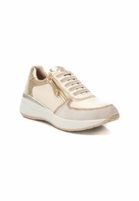 Zapatillas de color claro que presentan un tejido texturizado, cierre con cremallera y acentos metálicos. La suela es acolchada y ligeramente elevada.