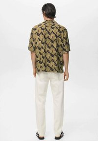 Chemise à manches courtes de couleur vert olive avec un motif géométrique, associée à un pantalon blanc, mettant en avant une coupe décontractée et une texture de tissu lisse.