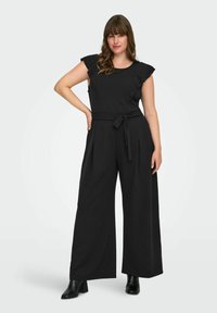 Svart jumpsuit med korta volangärmar, midjeband och vida ben. Tillverkad av ett slätt tyg, med vertikala veck och sidofickor.