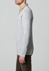 Szary pulower z długim rękawem i okrągłym dekoltem, z beżową koszulą z kołnierzykiem noszoną pod spodem. Prosty design o gładkiej fakturze.