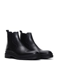 Bottines en cuir noir avec panneaux latéraux élastiques, bout rond et semelle en caoutchouc épaisse. Texture lisse avec un minimum de détails.