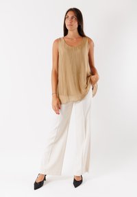 Top beige senza maniche in tessuto leggero, abbinato a pantaloni bianchi a gamba larga e tacchi neri a punta. Texture liscia e fluida.