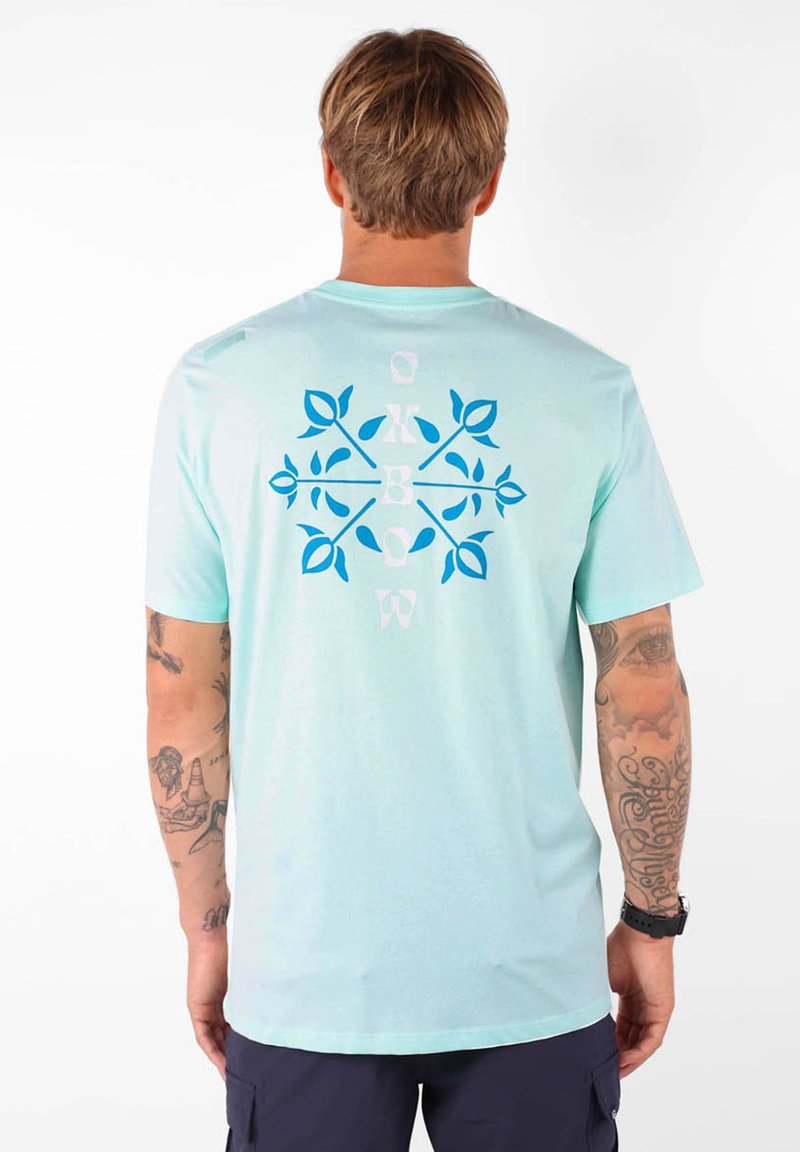 T-shirt bleu clair à manches courtes avec un design décoratif présentant des feuilles bleues et des lettres au dos ; tissu doux et coupe lâche.