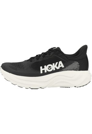 Черно бягащо обувки HOKA с бяла дебела подметка и голям бял лого на марката отстрани, показани на бял фон.