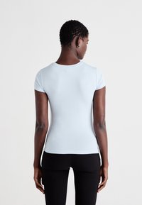 T-shirt fitted di colore azzurro chiaro, a maniche corte, con scollatura rotonda, texture liscia e finitura pulita in vita, indossato con pantaloni neri.