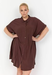 Abito button-up corto marrone a maniche corte con colletto, caratterizzato da una vestibilità morbida e spacchi laterali, realizzato in tessuto leggero.