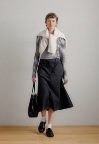 Μαύρη τζιν φούστα A-line, ριγέ μπλούζα με μακριά μανίκια, κρεμ πουλόβερ ριγμένο στους ώμους, μαύρη τσάντα και μαύρα παπούτσια με άσπρες κάλτσες.