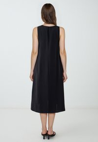 Abito nero senza maniche con taglio dritto, orlo a ginocchio, tessuto liscio e una cucitura posteriore discreta. Design minimalista senza fantasie.