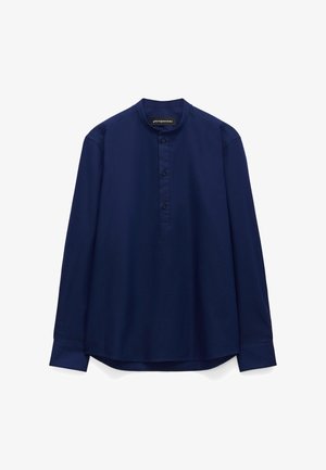 Granatowa koszula z długim rękawem z kołnierzykiem typu mandarynka i plisą na trzy guziki, zaprojektowana przez Adolfo Domingueza.