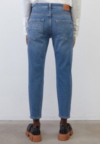 Jeans de talle alto en azul claro con un diseño de pierna recta. Cuenta con bolsillos traseros y un parche de logo de cuero marrón en la cinturilla.