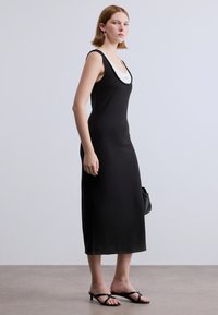 Μαύρο μίντι φόρεμα χωρίς μανίκια με στρογγυλή λαιμόκοψη, κατασκευασμένο από λείο ύφασμα. Διαθέτει λευκή λεπτομέρεια στη λαιμόκοψη. Φοριέται με μαύρα σανδάλια.