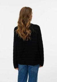 Maglione nero lavorato a maglia con un design testurizzato, maniche lunghe e spalle scese, abbinato a jeans in denim blu.