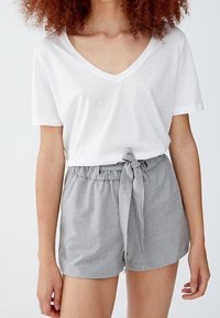 Femme portant un T-shirt blanc à col en V et un short gris taille haute avec une ceinture en tissu nouée en nœud à la taille.