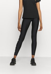 Czarne legginsy o gładkiej fakturze i dopasowanym kroju. Posiadają białe napisy wzdłuż boku. W połączeniu z prostą czarną koszulką i czarnymi butami.