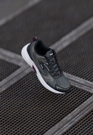 Gray athletic shoe with black and white accents, mesh material, rounded toe, padded collar, and logo detail on the tongue and side.