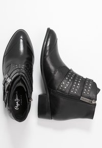 Černé kožené kotníkové boty s špičatými špičkami, dekorativními hroty a bočním zipem. Mají robustní podpatek a ozdobné pásky.