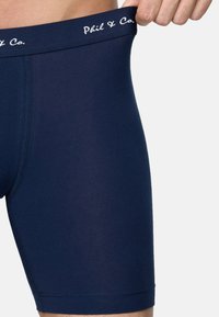 Marinblå boxershorts tillverkade av elastiskt material, med en vit logotyp på midjebandet och sömlös sömnad för komfort.