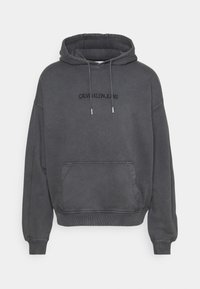 Sudadera gris con capucha, bolsillo tipo canguro, puños y dobladillo de canalé. Presenta el logo "CALVIN KLEIN JEANS" en negro en el pecho.