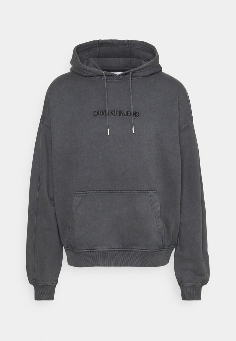 Sudadera gris con capucha, bolsillo tipo canguro, puños y dobladillo de canalé. Presenta el logo "CALVIN KLEIN JEANS" en negro en el pecho.