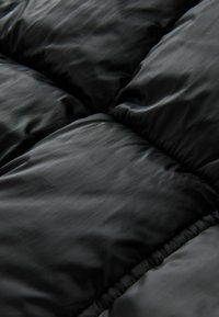 Țesătură quilted neagră cu o textură netedă, având secțiuni mari și pufoase și o strălucire subtilă, evidențiind ușurința și căldura sa.