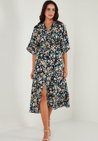 Floral-patterned dress in dark navy, featuring a V-neck, short sleeves, cinched waist, and side slit. Made from lightweight fabric.