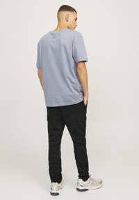Camiseta de algodón de color azul claro con mangas cortas, combinada con pantalones cargo negros con bolsillos laterales y zapatos con detalles en gris y plata.