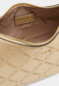 Interno di una borsa in pelle con azione in oro, caratterizzato da una texture liscia e lucida. Presenta un'etichetta con logo e una chiusura con zip e hardware metallico.