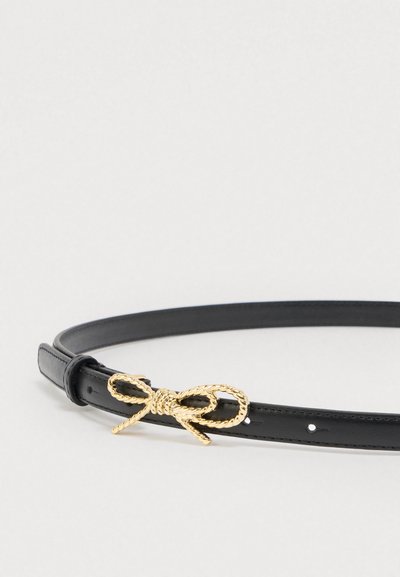 Curea neagră din piele, cu design subțire și cataramă aurie în formă de nod de frânghie. Dispune de mai multe găuri pentru ajustarea mărimii. Textură netedă.