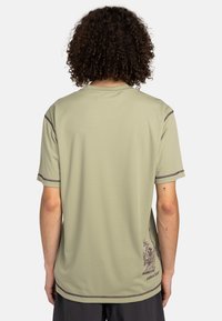 Light green athletic t-shirt with short sleeves, textured fabric, contrasting purple stitching, and a graphic detail on the lower back.