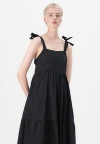 Melnas kokvilnas kleitas ar kvadrātveida dekoltē, daudzlīmeņu svārkiem un plecu saitēm. Raksturo gluda tekstūra un brīvi plūstošs dizains.