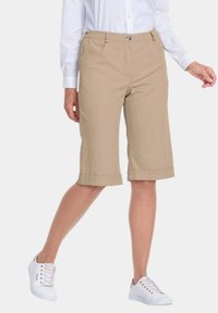 Shorts beiges de longueur genou avec un ourlet retroussé, en tissu de coton, dotés de poches avant et d'une taille plate, portés avec des baskets blanches.