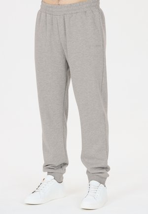 Mann trägt hellgraue Jogginghose mit elastischem Bund und Bündchen, kombiniert mit weißen Sneakers auf weißem Hintergrund.