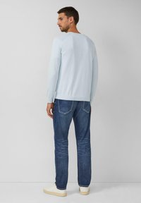 Lichtblauwe gebreide trui met een ronde hals, gedragen over donkerblauwe jeans. De outfit heeft een casual fit en ribbelboorden.