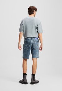 Chemise grise à manches courtes et shorts en denim bleu avec des bords effilochés. Bottines noires à la cheville. Design décontracté avec une coupe relaxée et poches arrière.
