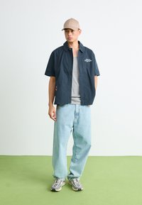 T-skjorte med korte ermer, mørk marineblå med broderi, grå tanktop under, lyseblå vide jeans og beige caps, brukt med grå joggesko.