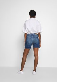 Pantalones cortos de mezclilla en azul oscuro con una cintura de altura media, diseño de cinco bolsillos, ligero desgastado y una etiqueta de marca de cuero marrón en la parte trasera de la cinturilla.