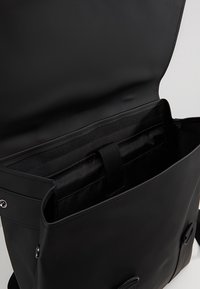 Sac messager en cuir noir à la texture lisse, avec fermeture à rabat et intérieur spacieux comprenant un compartiment rembourré et des poches supplémentaires.