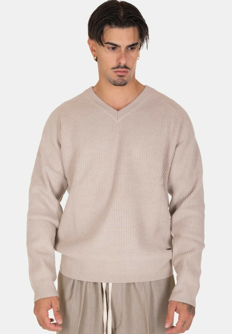 Maglione beige a coste con scollatura a V e maniche raglan, caratterizzato da una vestibilità rilassata e un tessuto testurizzato. Si abbina ai pantaloni chiari.