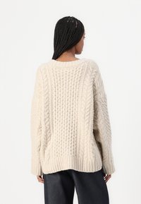 Chunky Strickpullover in hellbeige, mit Kabel- und Rippmustern, lockerer Passform, überschnittenen Schultern und rundem Halsausschnitt.
